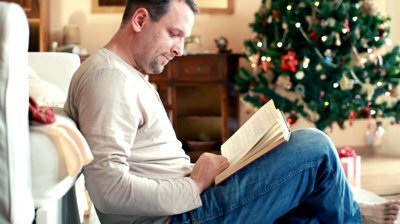 stock-footage-man-reading-book-christmas-tree-in-background Man reading a book with christmas tree in the background